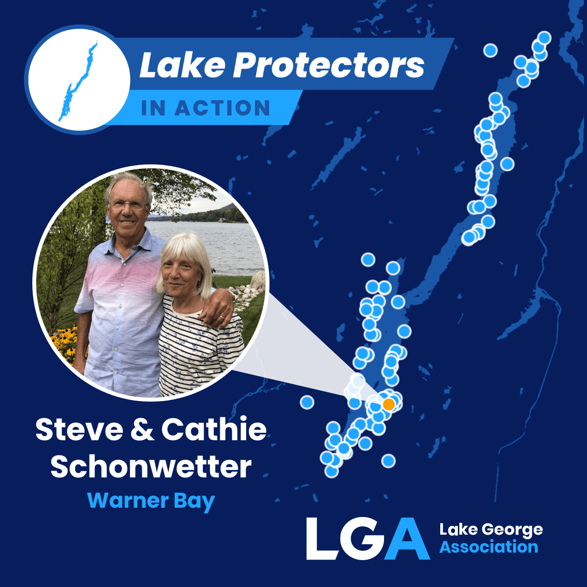 Man wearing a blue, pink, and white shirt with his arm around a woman wearing a white and blues strips shirt with flowers standing with Lake George in the background
